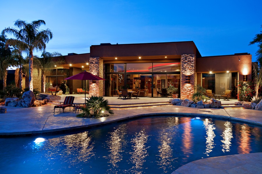 Outdoor entertainment area of a luxury home featuring a pool, lighting, and covert landscape speakers