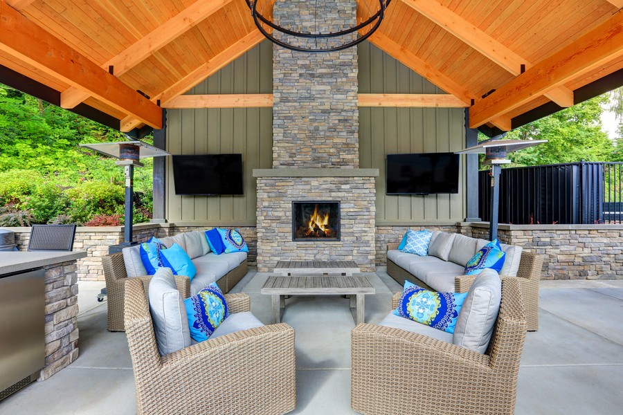 A patio setting with two outdoor TVs installed by the fireplace and seating area. 