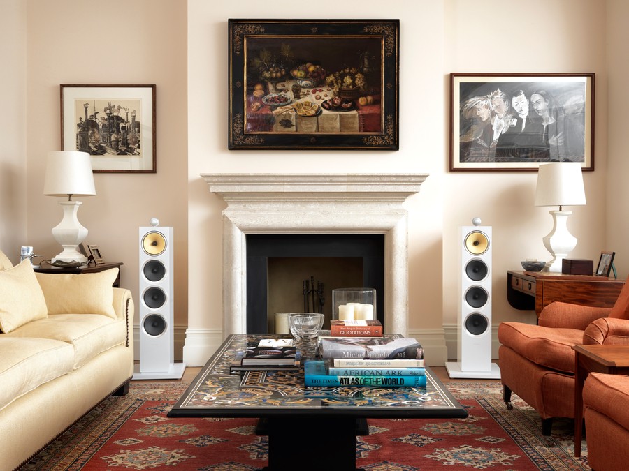 White Bowers & Wilkins high-end speakers standing on either side of a fireplace in a luxury living room. 