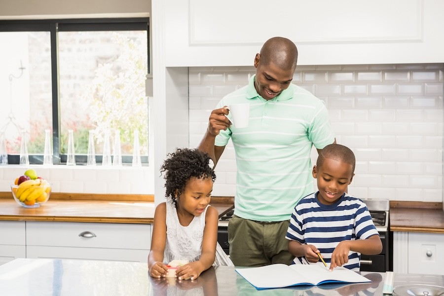 A father helping his children do homework in the kitchen.