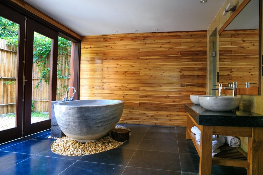 A bathroom with a soaking tub on rocks and a wooden wall.