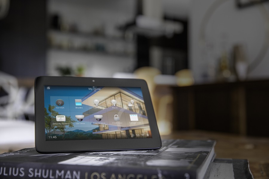 A smart home automation control tablet sits on top of books on a coffee table. 