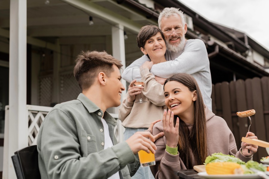 Outdoor family gathering with multiple generations enjoying food and drinks in a cozy backyard setting.