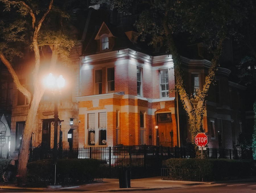 A stately brick home well-lit at night on a city street. 