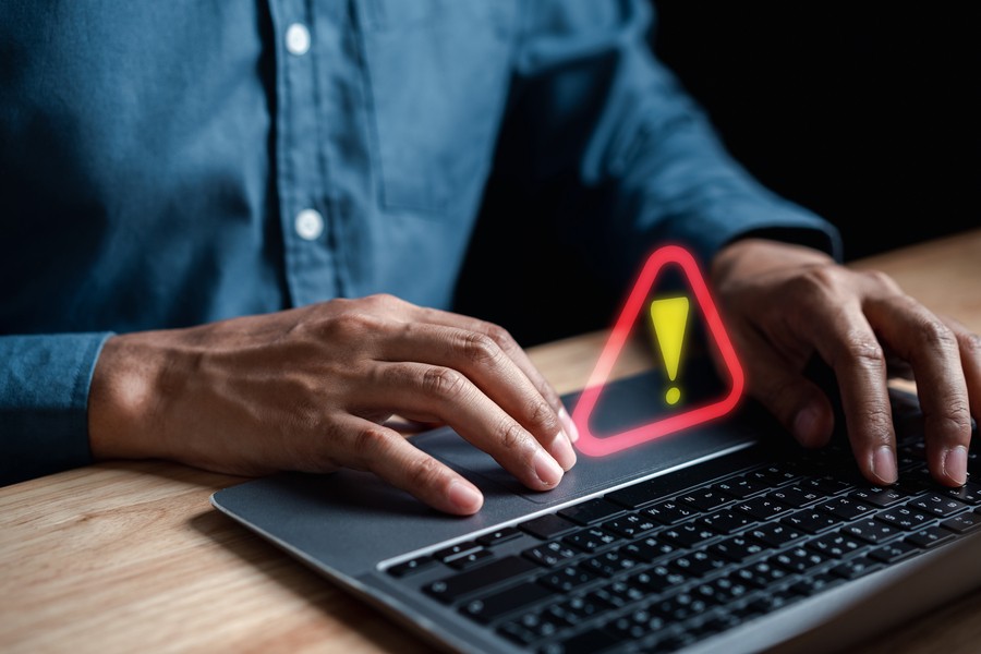 An exclamation point superimposed over an image of a man typing on a laptop. 