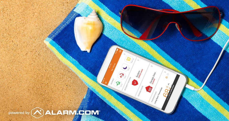 smartphone with an Alarm.com smart home security app interface sitting on a beach towel next to sunglasses.