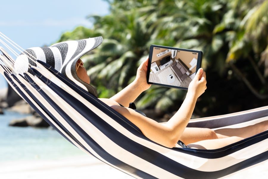 A woman in a hammock holding a tablet displaying a home security camera video feed.