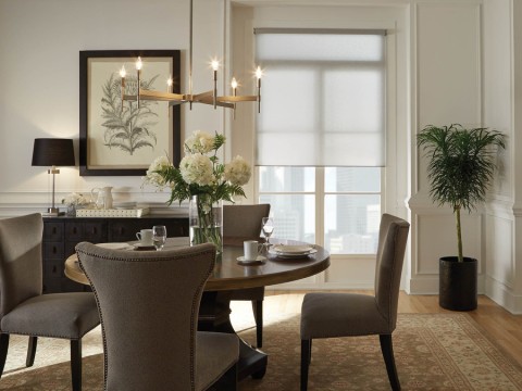 A kitchen dining table with a window in the background featuring roller shades.