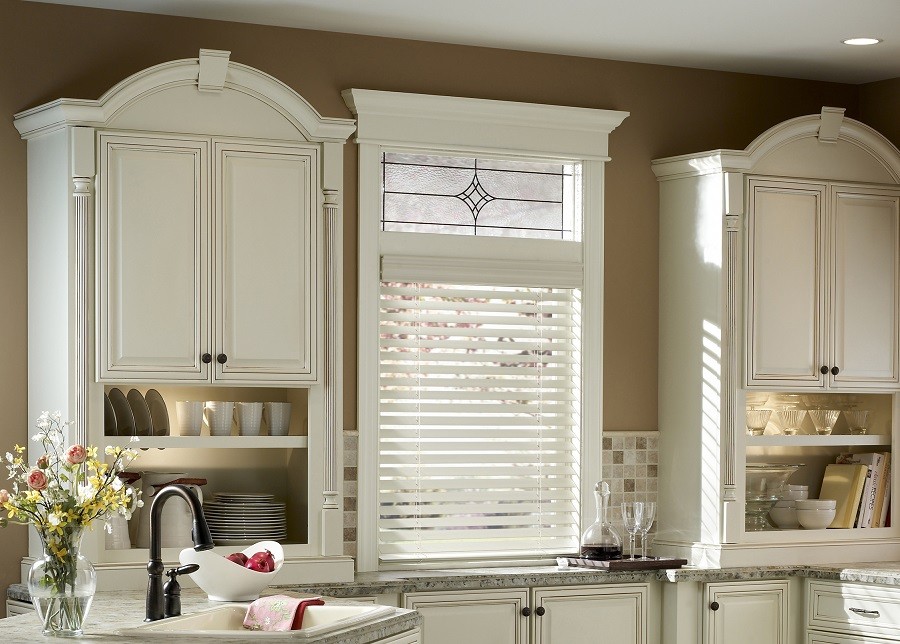 A kitchen with white cabinets and a small window with white blinds. 